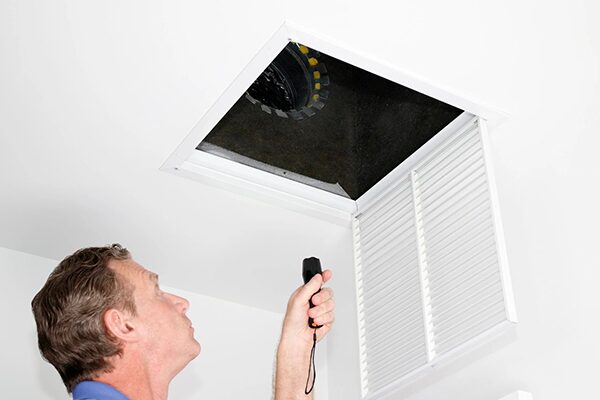 Male looking up into a ceiling air intake duct with a flashlight checking for maintenance